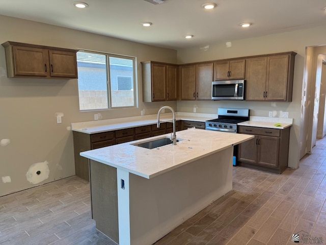 kitchen featuring light stone counters, sink, stainless steel appliances, and a center island with sink