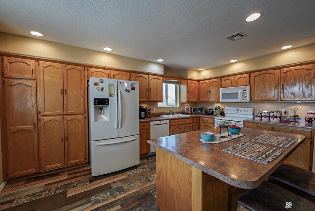 kitchen with visible vents, dark wood finished floors, brown cabinetry, white appliances, and a sink