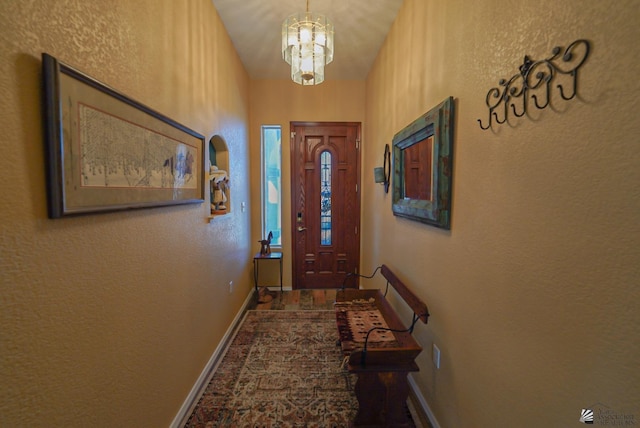 doorway to outside with an inviting chandelier, a textured wall, and baseboards