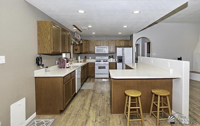 kitchen with white appliances, sink, light hardwood / wood-style flooring, a textured ceiling, and a kitchen bar