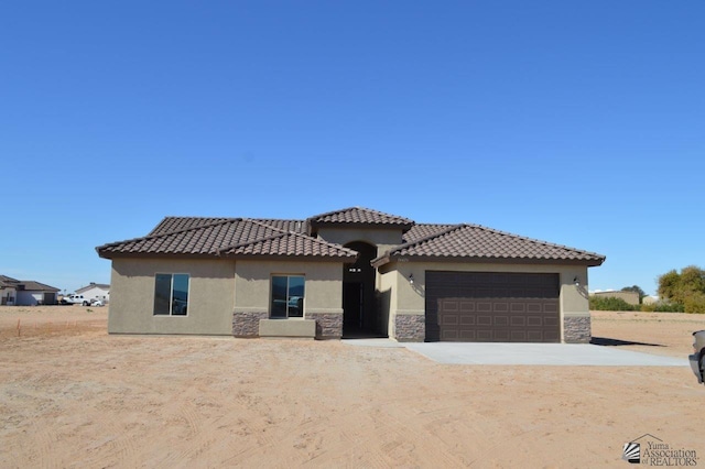 mediterranean / spanish-style house with a garage, stone siding, driveway, and stucco siding