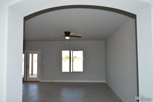 unfurnished room with baseboards, arched walkways, and ceiling fan