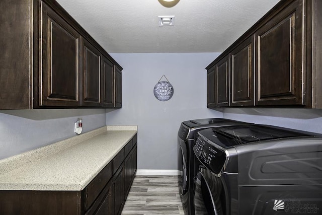 washroom with cabinets, washer and dryer, a textured ceiling, and light hardwood / wood-style flooring