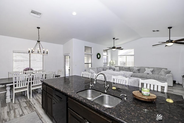 kitchen with decorative light fixtures, lofted ceiling, black dishwasher, sink, and dark stone counters