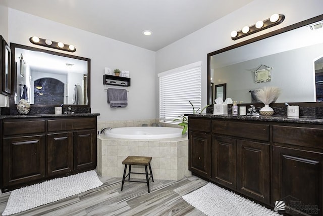 bathroom with hardwood / wood-style flooring, vanity, and a relaxing tiled tub