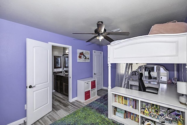 bedroom with wood-type flooring, a textured ceiling, ceiling fan, and ensuite bath