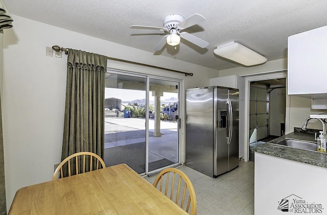 kitchen featuring stainless steel fridge, a textured ceiling, white cabinetry, and sink