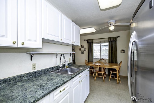 kitchen featuring stainless steel refrigerator, white cabinetry, sink, ceiling fan, and a textured ceiling