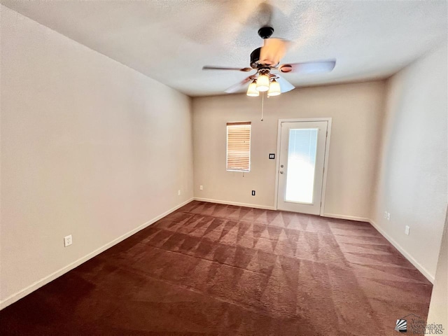 spare room featuring ceiling fan, dark carpet, and a textured ceiling