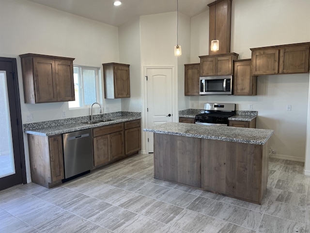 kitchen featuring a kitchen island, appliances with stainless steel finishes, decorative light fixtures, sink, and a high ceiling