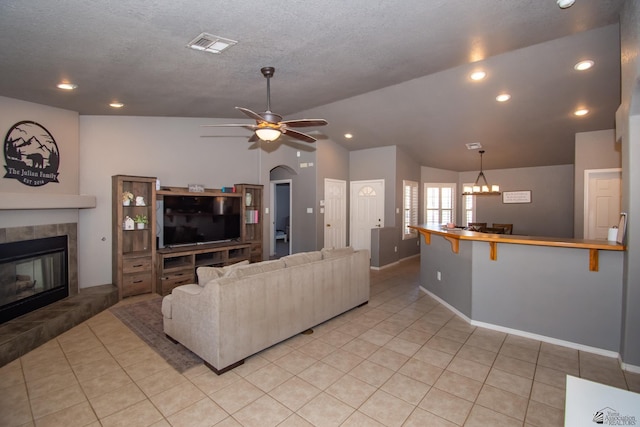 living area featuring light tile patterned floors, visible vents, a tile fireplace, lofted ceiling, and ceiling fan with notable chandelier