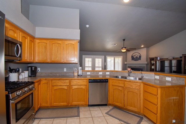 kitchen with a ceiling fan, a peninsula, stainless steel appliances, a fireplace, and a sink