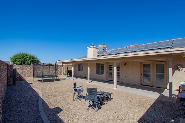 back of property with a fenced backyard, stucco siding, roof mounted solar panels, a trampoline, and a patio area