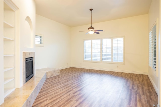 unfurnished living room with a tiled fireplace, ceiling fan, built in features, and light hardwood / wood-style floors