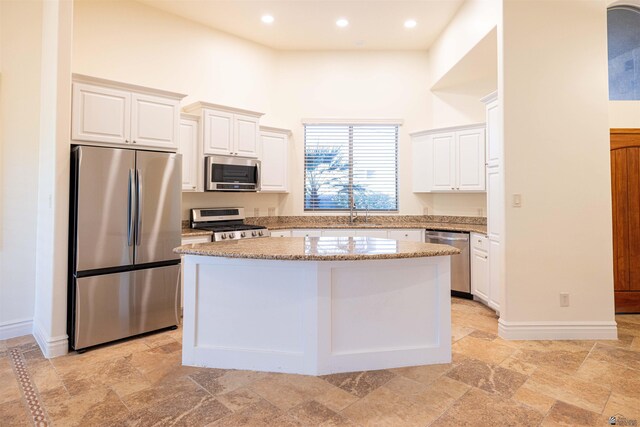 kitchen with light stone counters, a center island, white cabinets, and stainless steel appliances