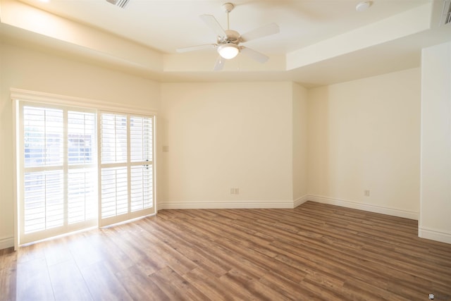 empty room featuring ceiling fan, wood-type flooring, and a tray ceiling