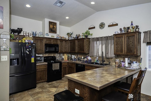 kitchen with dark brown cabinetry, backsplash, kitchen peninsula, a kitchen bar, and black appliances