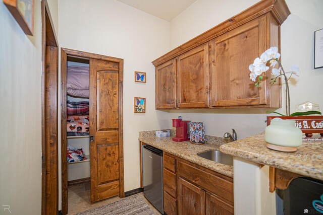 kitchen with light stone counters, sink, light tile patterned flooring, and stainless steel dishwasher