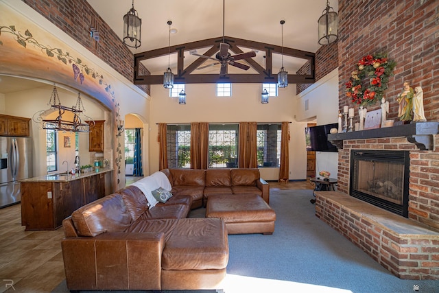 carpeted living room with ceiling fan, sink, beamed ceiling, a fireplace, and a high ceiling