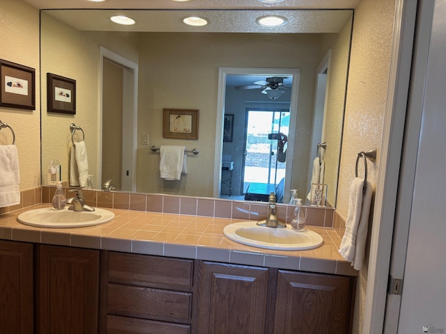 full bathroom featuring a textured wall, double vanity, a sink, and a ceiling fan