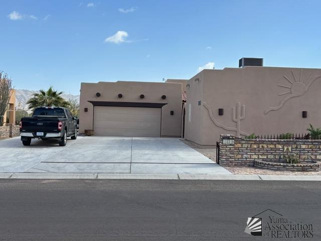 southwest-style home featuring driveway, an attached garage, central AC unit, and stucco siding