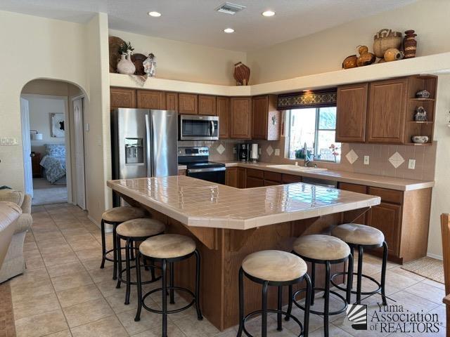 kitchen with arched walkways, appliances with stainless steel finishes, visible vents, and decorative backsplash