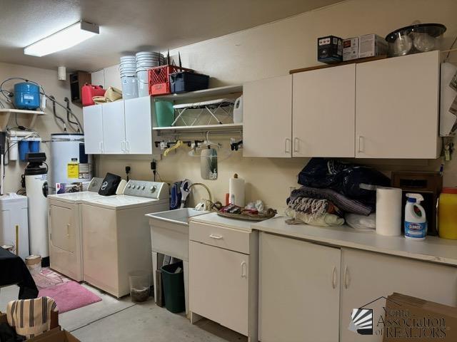 clothes washing area with water heater, washer and clothes dryer, and cabinet space