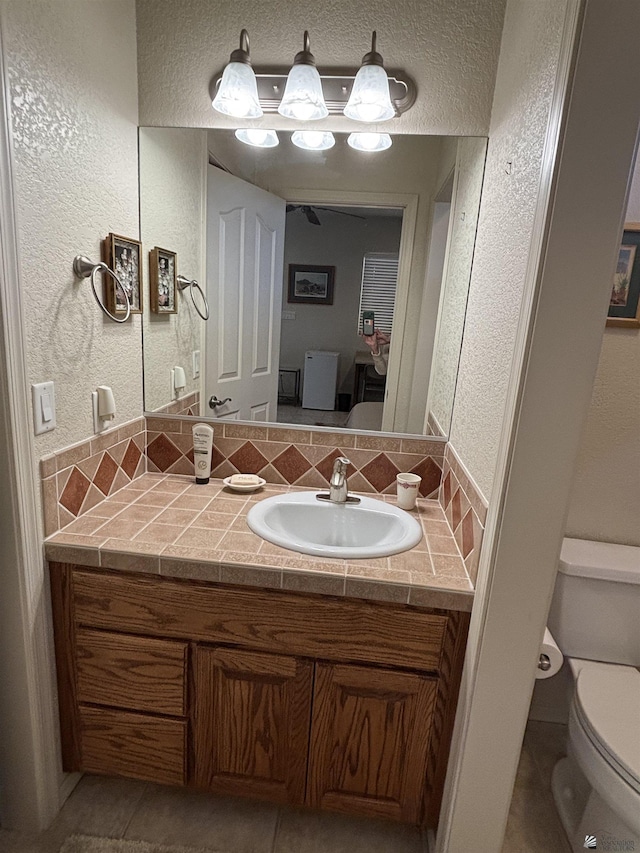 bathroom with a textured wall, vanity, and toilet