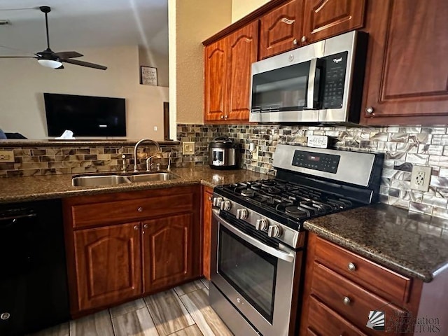 kitchen with sink, ceiling fan, dark stone countertops, appliances with stainless steel finishes, and tasteful backsplash