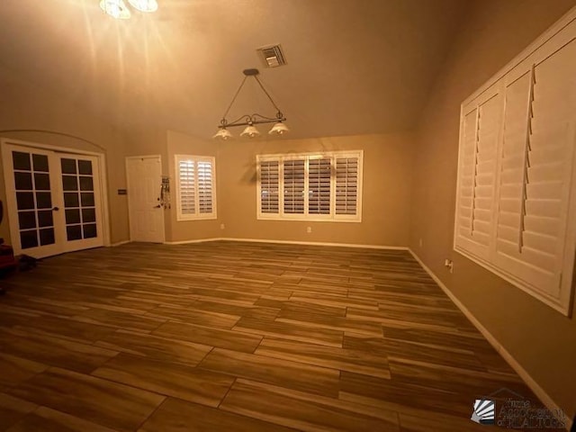 spare room with hardwood / wood-style floors, an inviting chandelier, lofted ceiling, and french doors