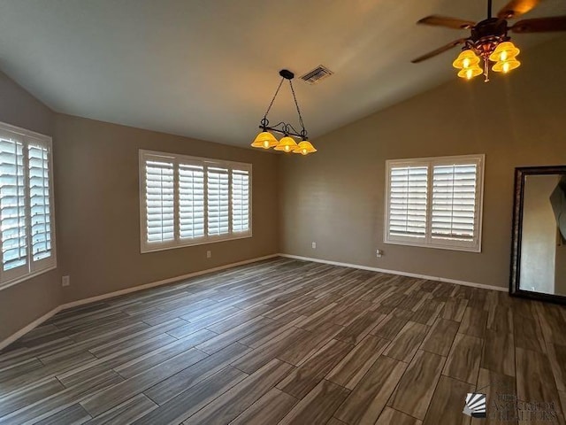 spare room with ceiling fan with notable chandelier, a healthy amount of sunlight, dark hardwood / wood-style flooring, and vaulted ceiling