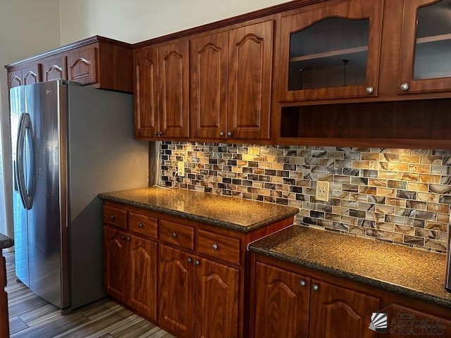 kitchen with stainless steel fridge, backsplash, dark stone counters, and dark wood-type flooring