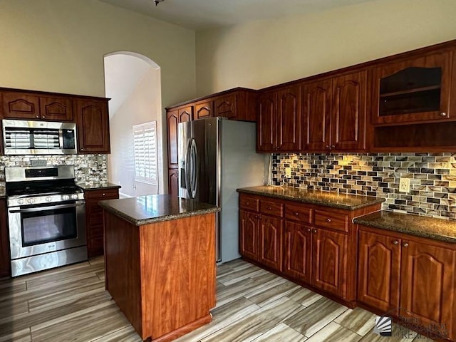 kitchen featuring stainless steel appliances, tasteful backsplash, dark stone countertops, light hardwood / wood-style floors, and a kitchen island