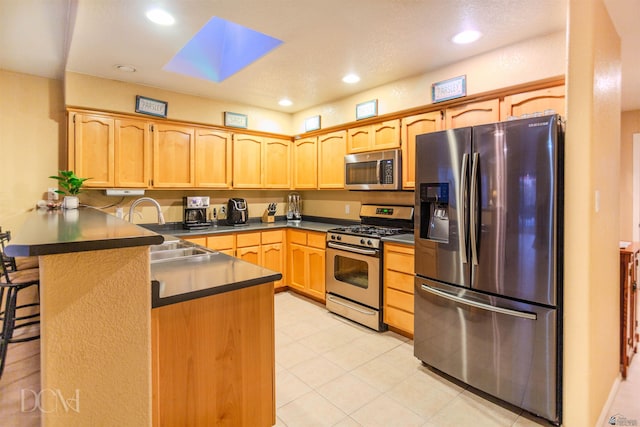 kitchen with a skylight, sink, a kitchen breakfast bar, kitchen peninsula, and appliances with stainless steel finishes