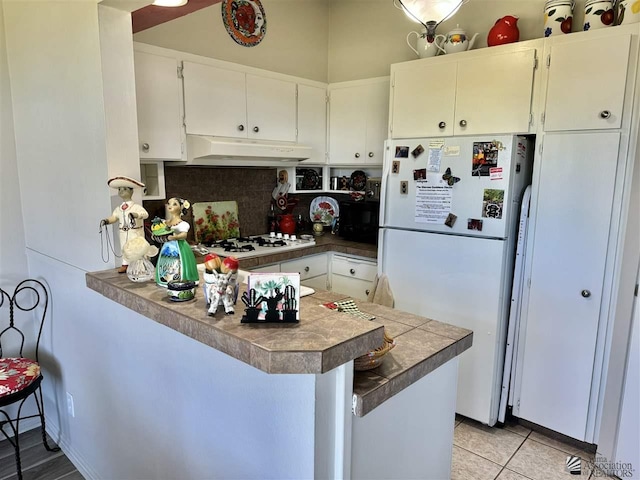 kitchen featuring under cabinet range hood, a peninsula, white appliances, white cabinetry, and decorative backsplash