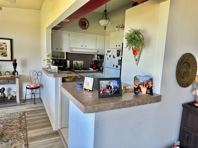 kitchen with decorative light fixtures, light wood finished floors, tile counters, freestanding refrigerator, and a peninsula