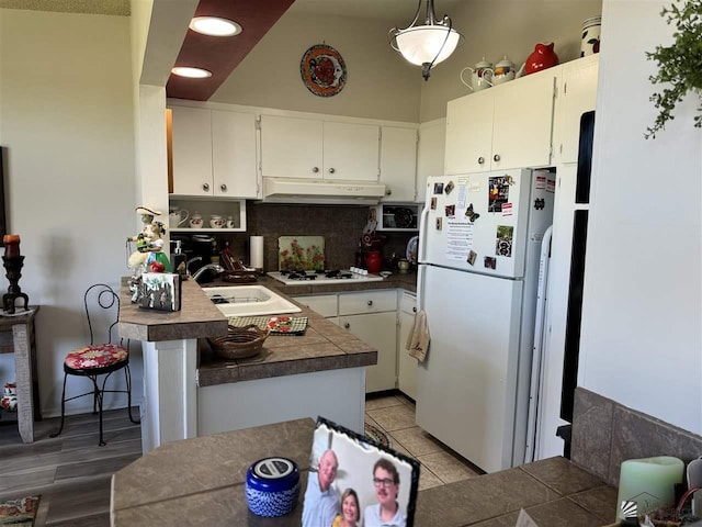 kitchen with white cabinetry, a sink, a peninsula, white appliances, and under cabinet range hood