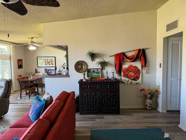 living room featuring visible vents, baseboards, dark wood-style floors, ceiling fan, and a textured ceiling