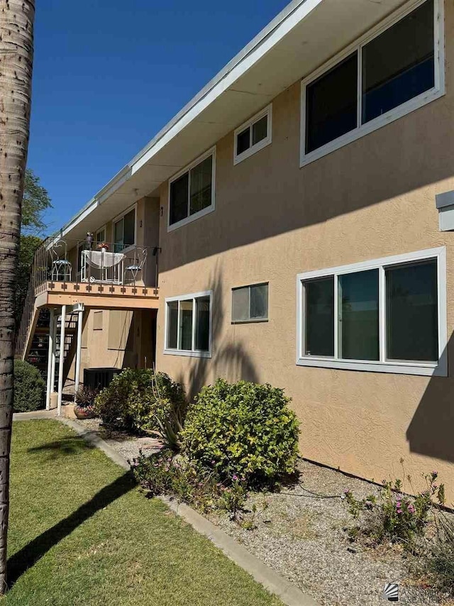 rear view of house featuring stairs, a yard, and stucco siding