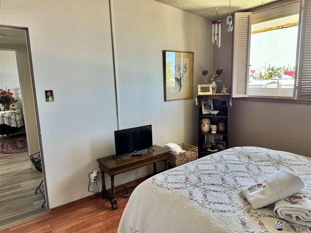 bedroom with a textured ceiling, baseboards, and wood finished floors