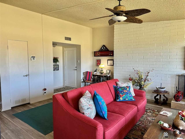 living room with a textured ceiling, dark wood finished floors, visible vents, and a ceiling fan