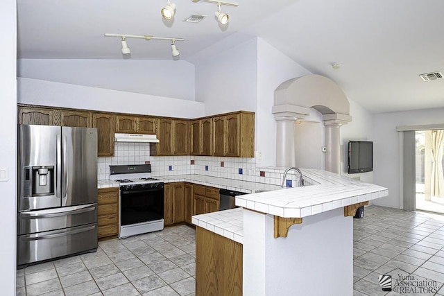 kitchen with tile countertops, light tile patterned floors, kitchen peninsula, stainless steel appliances, and backsplash