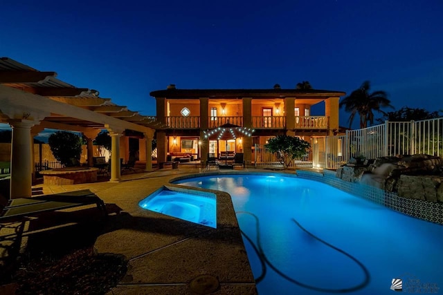 pool at night with an in ground hot tub, a pergola, and a patio area