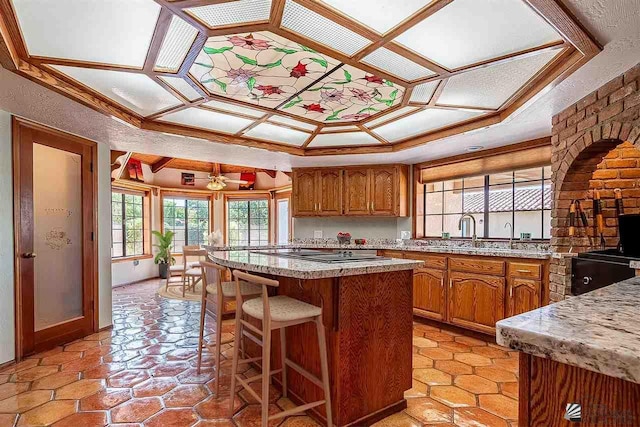 kitchen featuring a kitchen island, a breakfast bar, sink, black electric stovetop, and a raised ceiling