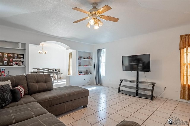 living room featuring a textured ceiling, built in shelves, light tile patterned floors, and ceiling fan with notable chandelier