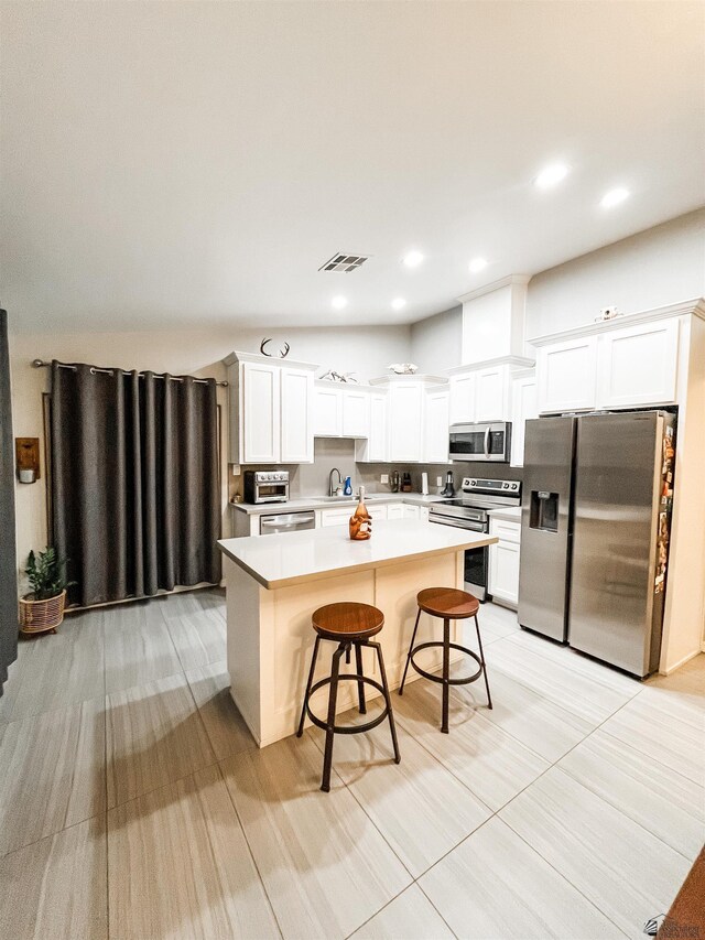 kitchen with a kitchen breakfast bar, stainless steel appliances, sink, white cabinets, and a center island