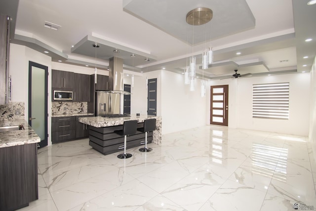 kitchen featuring dark brown cabinetry, hanging light fixtures, appliances with stainless steel finishes, and a tray ceiling