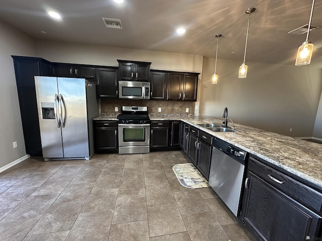 kitchen with appliances with stainless steel finishes, sink, backsplash, hanging light fixtures, and light stone countertops