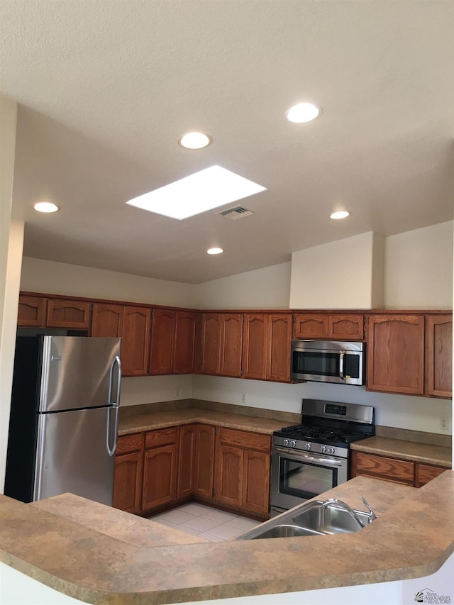 kitchen featuring sink, light tile patterned floors, stainless steel appliances, and vaulted ceiling with skylight