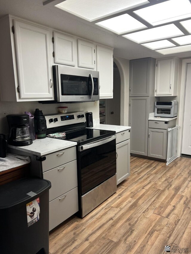 kitchen with stainless steel appliances, white cabinetry, and light hardwood / wood-style floors